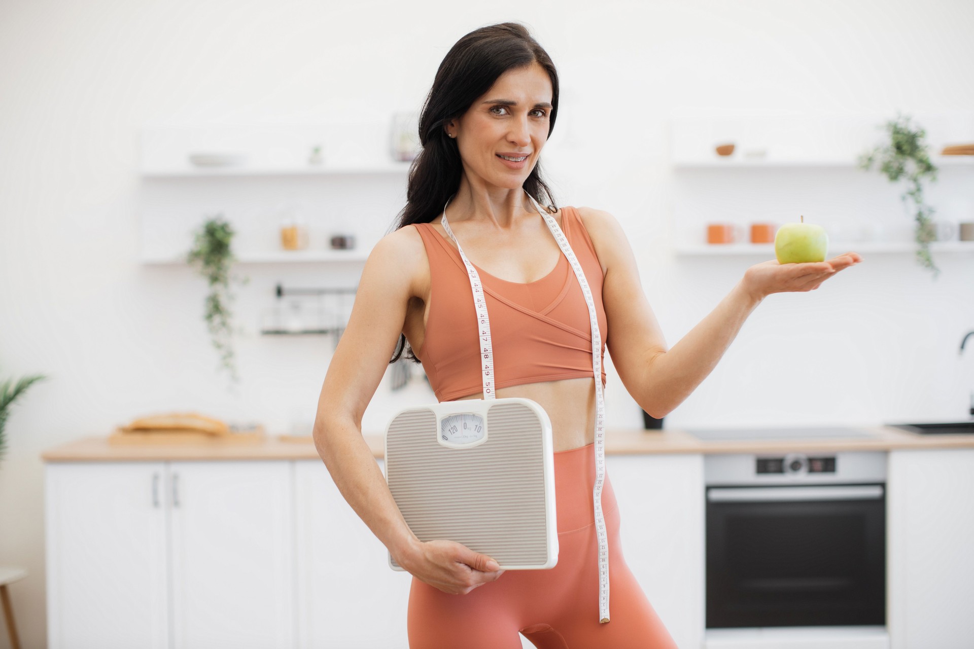 Health coach with measuring tape, scales and apple at home